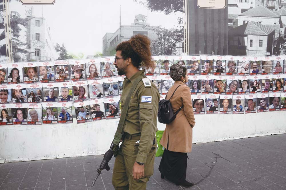圖為人們走過一堵牆，牆上掛著大約240名人質的照片。圖／美聯社